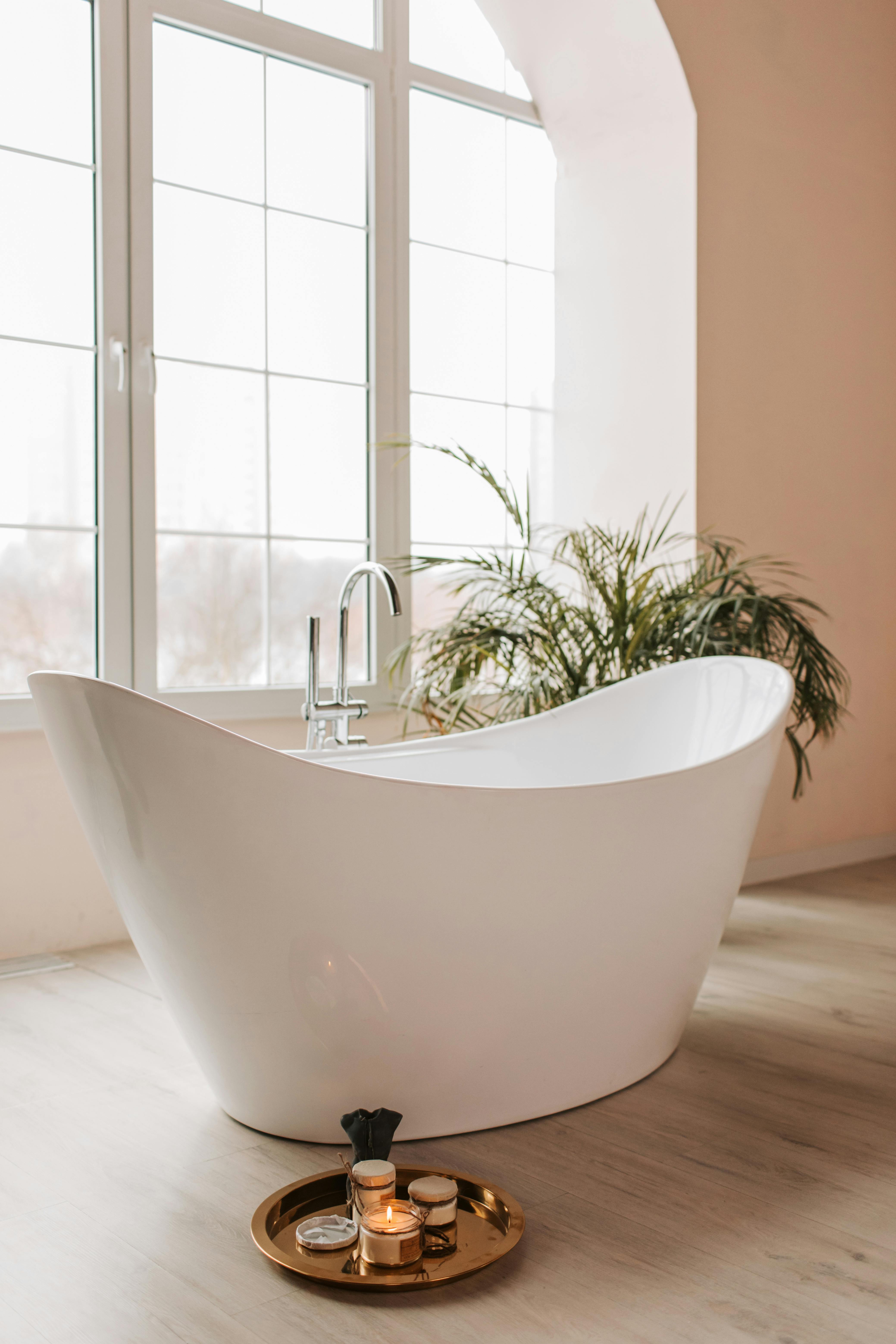 A stylish white bathtub in a minimalist bathroom with natural lighting and houseplants.
